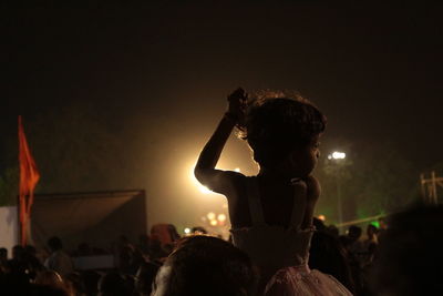 Rear view of girl with crowd enjoying music concert at night