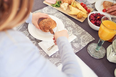 High angle view of woman hand cutting bread in plate on table 