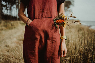 Midsection of woman standing by flowering plant on field