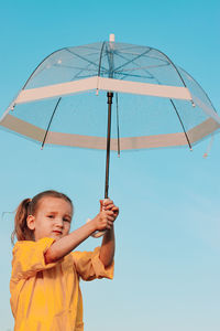 Girl holding umbrella against clear blue sky