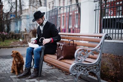 Full length of man sitting on bench with dog outdoors