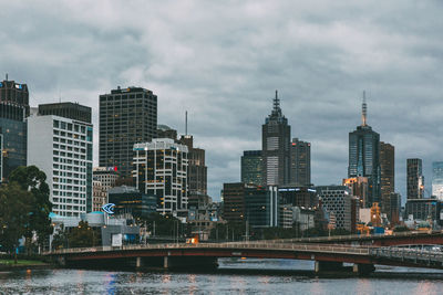 Modern buildings by river against sky in city