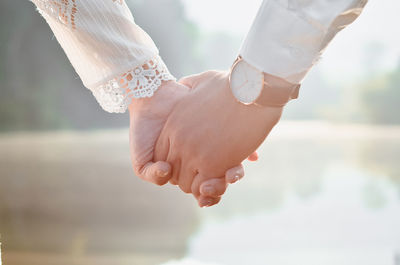 Close-up of couple holding hands against lake