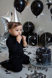 Boy stands next to a festive black cake and balloons