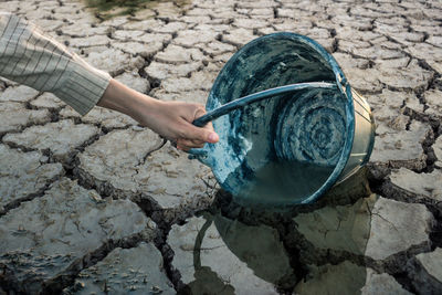 Cropped hand holding bucket on drought field
