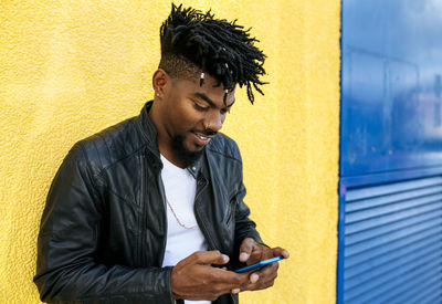Close-up of mid adult man with locs using mobile phone while standing against wall