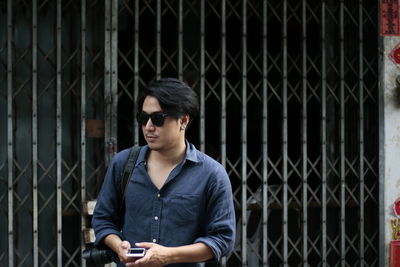 Young man wearing sunglasses while standing against chainlink fence