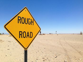 Road sign on barren landscape against clear blue sky
