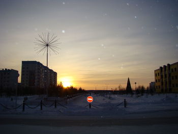 Silhouette buildings by street against sky during sunset