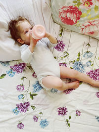 High angle view of girl drinking milk while lying down on bed