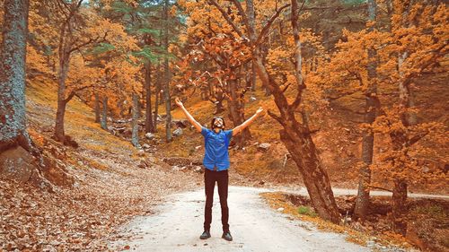 Man throwing leaves while standing on footpath in forest 