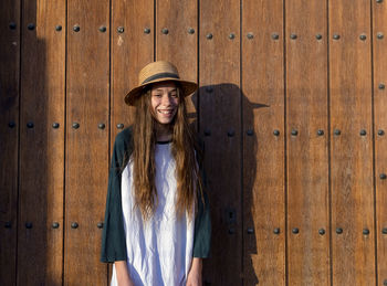 Smiling young woman standing against wooden door