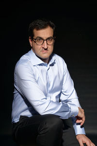 Portrait of young man sitting against black background