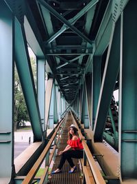 Portrait of woman sitting on railing under bridge