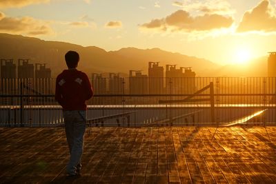 Rear view of silhouette man standing on railing against sunset sky