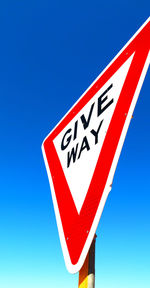 Low angle view of road sign against clear blue sky