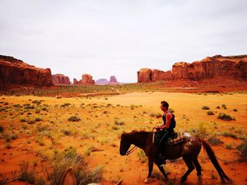 Side view of man riding horse at monument valley against sky