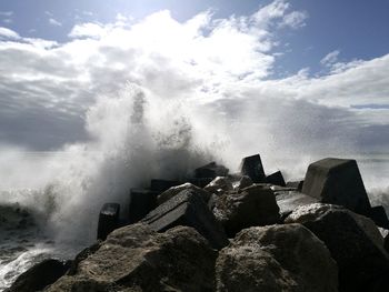 Waves splashing on rocks by sea against sky