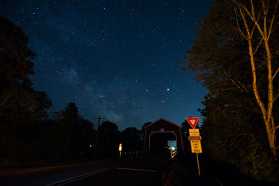 Covered bridge by trees against star field at night