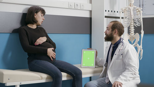 Doctor with digital tablet discussing with pregnant woman in hospital