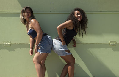 Full length of two young women laughing against green wall