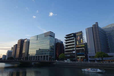 Modern buildings by river against sky in city