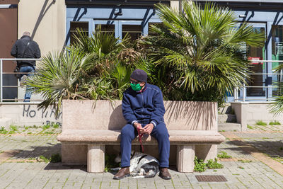 Full length of man sitting on seat against footpath