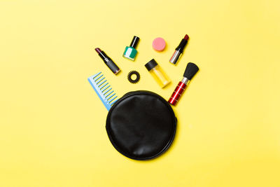 Directly above shot of purse with beauty products over yellow background