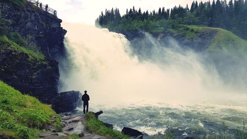 Rear view of man looking at waterfall against mountain