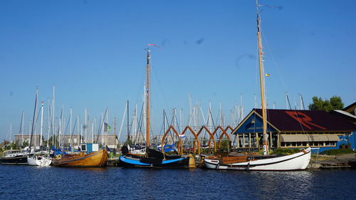 Sailboats moored at harbor against clear blue sky