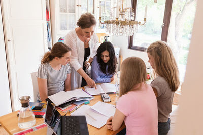 Woman assisting teenage girls in doing homework at home