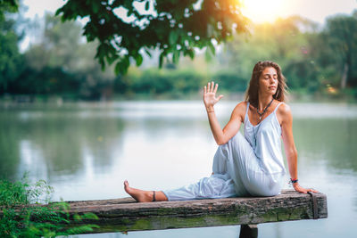 Woman doing yoga while sitting on pier at lake