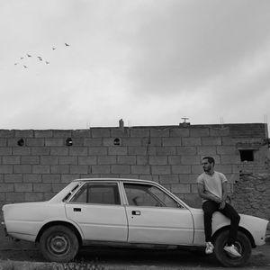 Young man sitting on car against surrounding wall