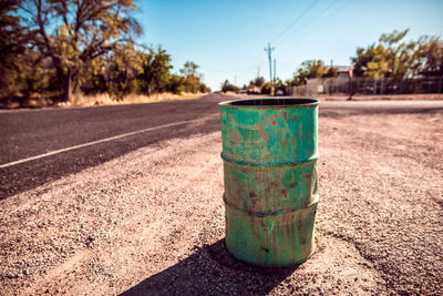 Abandoned green drum by road on sunny day