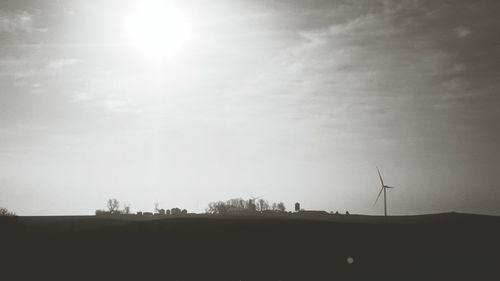 Silhouette of wind turbines on field against sky