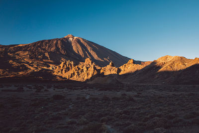 Scenic view of arid landscape against clear blue sky