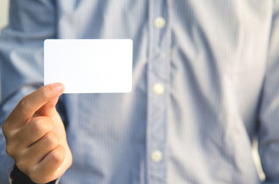 Midsection of man holding blank business card against white background