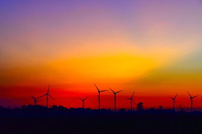 Silhouette wind turbines on land against sky during sunset