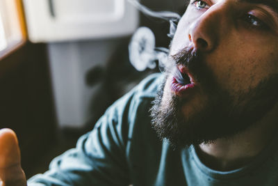 Close-up of bearded man exhaling smoke while smoking marijuana joint at home