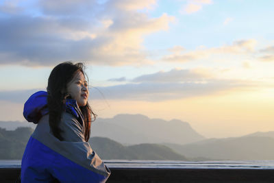 Young woman standing by sea against sky during sunset