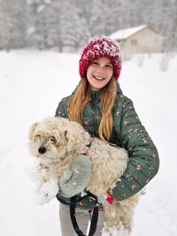 Portrait of a smiling young girl holding up her extremely shaggy dog whose paws are caked in snow.