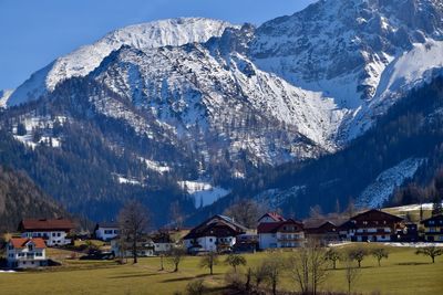 Scenic view of landscape with houses against snowcapped mountains and sky