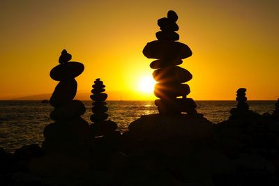 Silhouette stone stacks at sea shore against orange sky