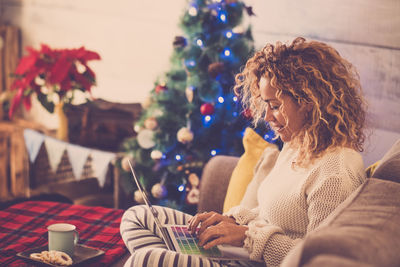 Midsection of woman holding coffee while sitting on christmas tree