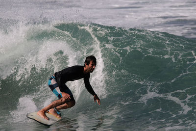 Full length of shirtless man surfing in sea