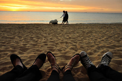 Low section of friends against man and woman with dogs at beach during sunset