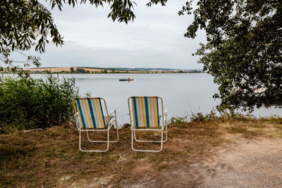 Chair on lakeshore against sky