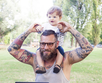 Smiling bearded man giving piggyback ride to son on field 