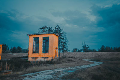 Abandoned house on field by trees against sky