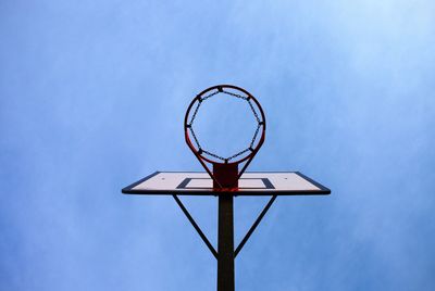 Old neglect basketball backboard with rusty hoop above street court. blue sky in background.